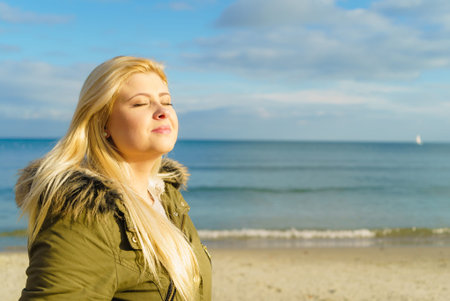 Leisure, spending free time outside, healthy walks concept. Woman wearing warm jacket relaxing on beach near sea, cold sunny dayの写真素材