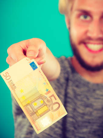 Riches, finances concept. Man holding money in 50 euro bills, studio shot on blue backgroundの写真素材