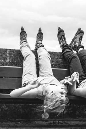 Young people friends in training suit with roller skates. Woman and man relaxing lying on bench outdoor.の写真素材