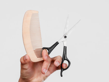 Style and fashion. Male hand of hairstylist barber holds scissors and wooden comb, creating hairdo...