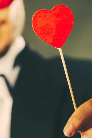 Valentines day. Love concept. Holidays and celebration. Elegant young guy wearing suit white shirt bow tie holding heart stick in handの写真素材