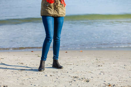 Leisure, spending free time outside, healthy walks concept. Woman wearing warm jacket relaxing on beach near sea, cold sunny dayの写真素材