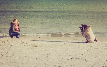 Photo session, professional concept. Woman posing at beach and photographer taking her pictures near seaの写真素材