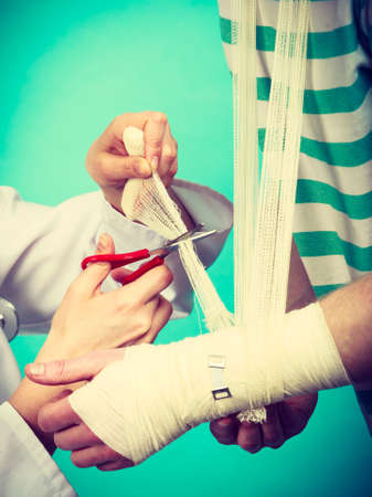 Medicine and healthcare. Female doctor bandaging male hand sprained wrist. Young man visiting medical professionalist.の写真素材