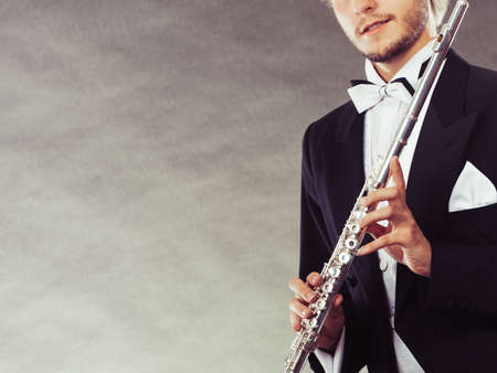 Classical music, passion and hobby concept. Elegantly dressed musician man holding flute. Studio shot on dark grey backgroundの写真素材