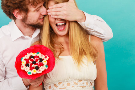 Handsome man giving woman candy bunch flowers. Young boyfriend with surprise present gift for...