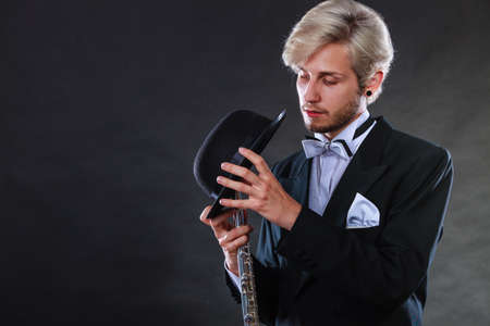 Classical music, passion, hobby concept. Elegantly dressed musician man holding flute and black fedora hat. Studio shot on dark backgroundの写真素材