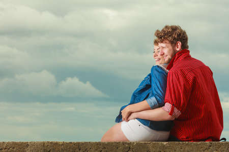 Loving couple spending leisure time together at beach sitting on sea shore hugging side viewの写真素材