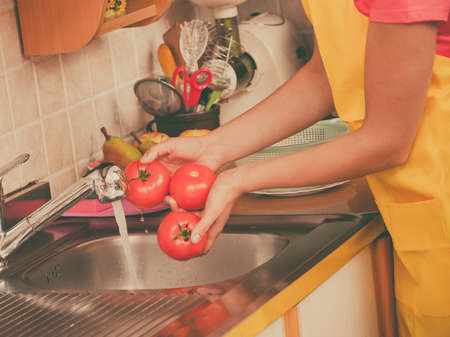 Woman hands washing fresh vegetables tomatoes in kitchen under water stream, preparation salad vegetarian mealの写真素材