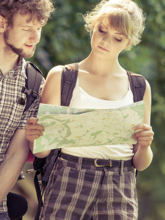Man and woman tourists backpackers reading map on trip. Young couple hikers searching looking for...
