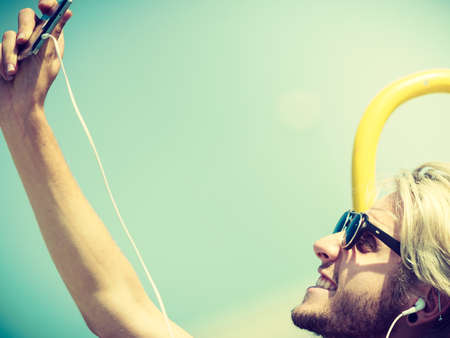 Contacts, technology, self-esteem concept. Young blonde man on vacations using his smartphone to take cool selfie shotの写真素材