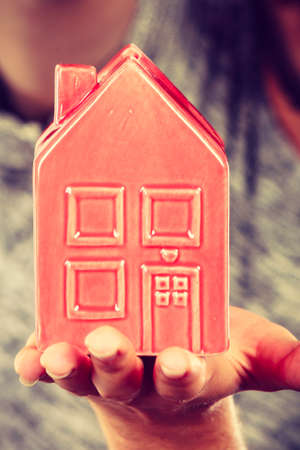 Household savings, housekeeping concept. Man holding tiny red statue in shape of house. Studio shot on blue backgroundの写真素材