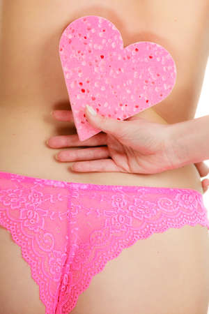 Skincare hygiene health and body treatment. Closeup sensual woman wearing pink panties holding heart shaped bath sponge in hand next to hips, isolated on whiteの写真素材