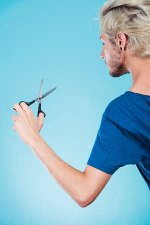 Coiffure hairstyle and haircut. Young cool guy holding special shears tool for work of hairdresser, on blueの写真素材