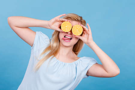 Healthy diet, refreshing food full of vitamins. Woman holding sweet delicious citrus fruit, lemon two halfs pretending it is eyeglassesの写真素材