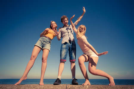 Friendship happiness summer holidays concept. Group of friends boy two girls having fun outdoor stretching arms celebrating, wide angle viewの写真素材