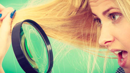 Haircare and hairstyling, bad effects of bleaching concept. Shocked blonde woman looking at her damaged, split hair ends through magnifying glass.の写真素材