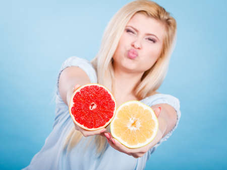 Woman smiling girl holding two halfs of grapefruit red and yellow citrus fruit in hands, on blue. Healthy food, dieting concept.の写真素材
