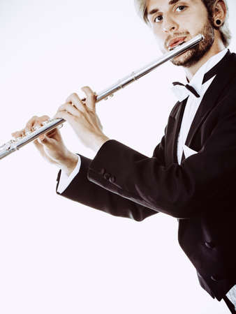 Classical music study concept. Male flutist musician performer playing flute. Young elegant man wearing tailcoat holds instrumentの写真素材