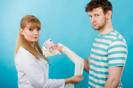 Corruption in healthcare industry. Female doctor bandaging male hand. Man giving money to woman. Bribery in medicine.の写真素材