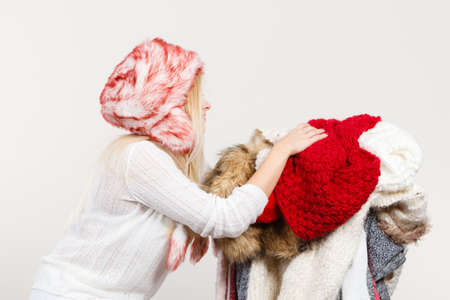 Accessories and clothing for cold days, fashion concept. Blonde woman in winter warm furry hat russian style holding big pile of clothesの写真素材