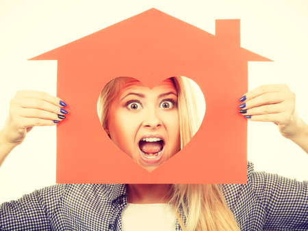 Charity, real estate and family home concept - Happy funny teen girl holding red paper house with heart shape, toned imageの写真素材