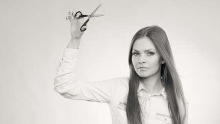 Beauty danger haircut coiffure care concept. Smiling lady showing tools. Young cheerful irresponsible hairdresser waving around razor sharp scissors, holding special chunking texturizing shearsの写真素材