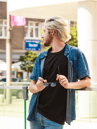 Men fashion, urban style clothing concept. Hipster guy standing on city street wearing jeans outfit...