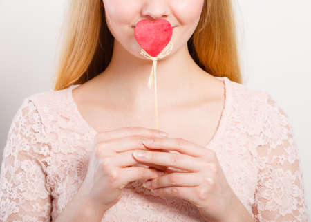 Quietly about love and feelings. Lovely charming blonde female covering her mouth by little small heart on stick.の写真素材