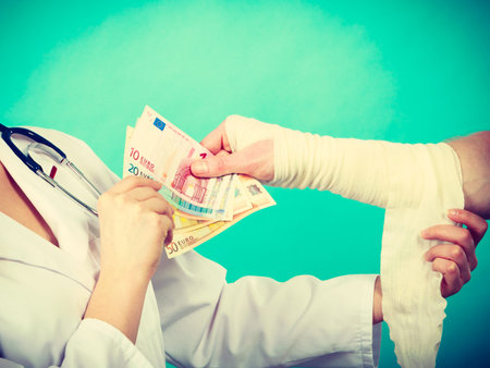 Corruption in healthcare industry. Female doctor bandaging male hand. Man giving money to woman. Bribery in medicine.の写真素材