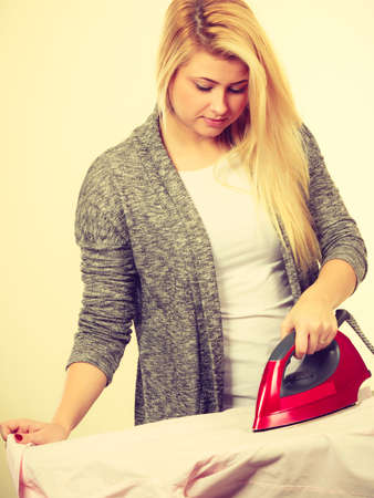 Household duties, taking care of clothes concept. Happy woman standing behind board ironing clothingの写真素材