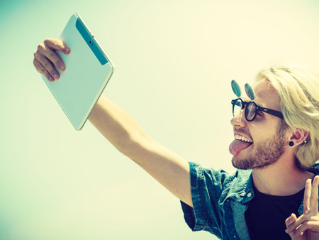 Contacts, technology, self-esteem concept. Young blonde man on vacations using his tablet to take...