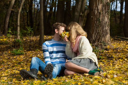 Love relationship dating and people concept - couple hiding behind leaves kissing in autumn parkの写真素材