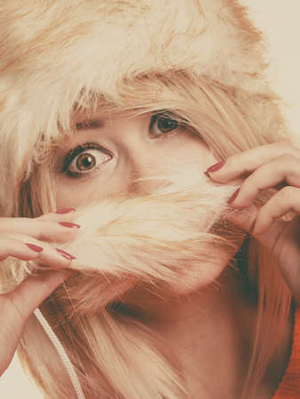 Outfit for cold days ideas, fashion and clothing concept. Attractive smiling blonde woman wearing furry winter hat, hiding behing furr tailの写真素材