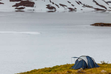 Camping with tent on snowfield with view on snow capped mountains and frozen lake in Norway.の写真素材
