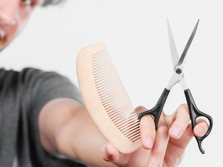Style and fashion. Male hand of hairstylist barber holds scissors and wooden comb, creating hairdo...