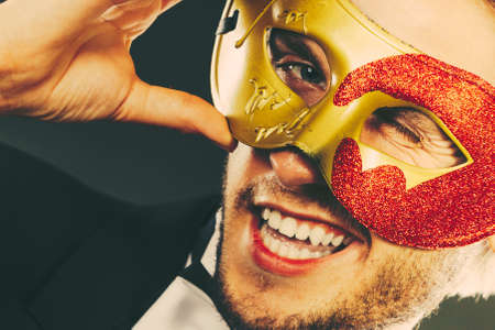 Holidays, people and celebration concept. Young guy wearing carnival venetian mask, on dark.の写真素材