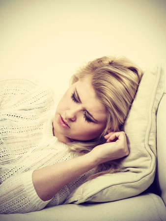 Negative human face expressions concept. Sick, sad, depressed woman lying on couch feeling very unwell.の写真素材