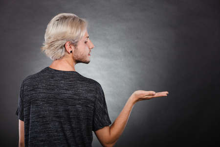 Young man showing presenting. Stylish guy holding empty hand palm copy space for product. Fashion, advertising concept. Back viewの写真素材