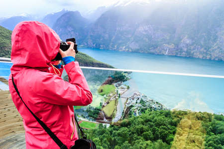 Tourism and travel. Woman tourist nature photographer taking photo with camera, enjoying Aurland fjord landscape from Stegastein lookout, Norway Scandinavia.の写真素材