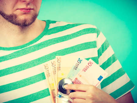 Corruption in medicine. Female doctor with stethoscope checking heart beating. Male bandaged hand with banknotes euro money.の写真素材