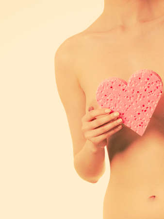 Skincare hygiene health and body treatment. Sensual naked woman with perfect skin holding orange heart shaped bath sponge in hands, covering her breast. Toned imageの写真素材