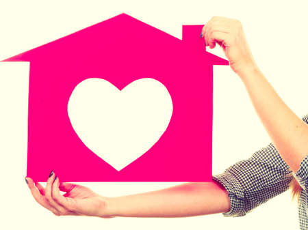 Ownership and property concept. Happy woman holding pink paper house with hole in heart shape, loving new home.の写真素材