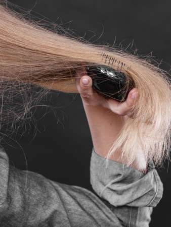 Everyday hygiene and care about good look. Back view of blonde casual girl combing her long straight hair. Woman using black comb hairbrush.の写真素材