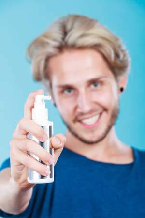 Hairdo haircare and makes hairstyle concept. Handsome young guy, fashion blonde metrosexual model applying spray cosmetic to his hairの写真素材