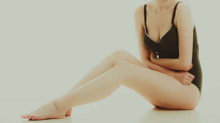 Depilation, epilation, clean, fresh skin concept. Woman in black swimsuit underwear sitting on floor, showing and touching her legs.の写真素材