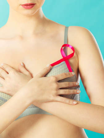 Health care, medicine and breast cancer awareness concept. Young woman in bra with pink ribbon symbol against blueの写真素材
