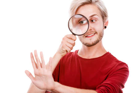 Narcissist, self absorption concept. Male holding magnifying glass looking at hands fingers nails obsessing about cleanliness, isolated on whiteの写真素材