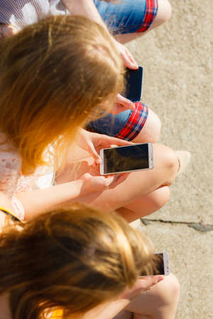 Friends texting using mobile phones outdoor. Women and man browsing internet on smartphone. Summer relax.の写真素材