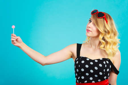 Woman attractive cheerful blonde girl holding little lollipop candy in hand. Sweet food and enjoying concept. Studio shot blueの写真素材